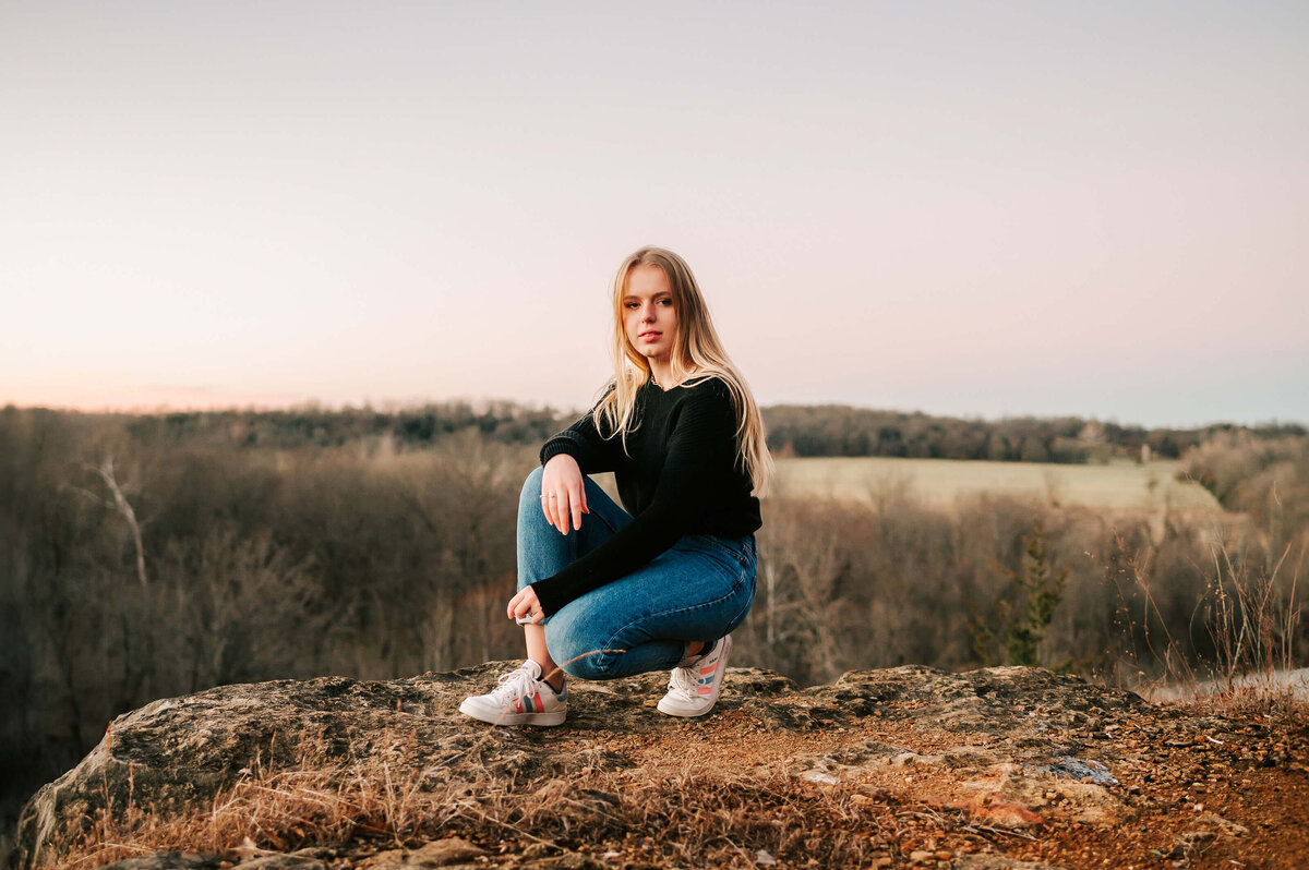 senior picture in high school senior girl squatting on cliffside in Branson