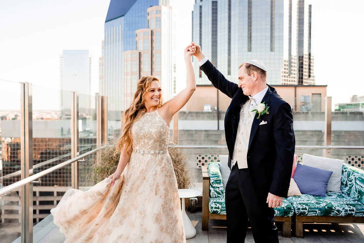 Bride and groom twirling on top of the Noelle hotel with the Nashville skyline behind them
