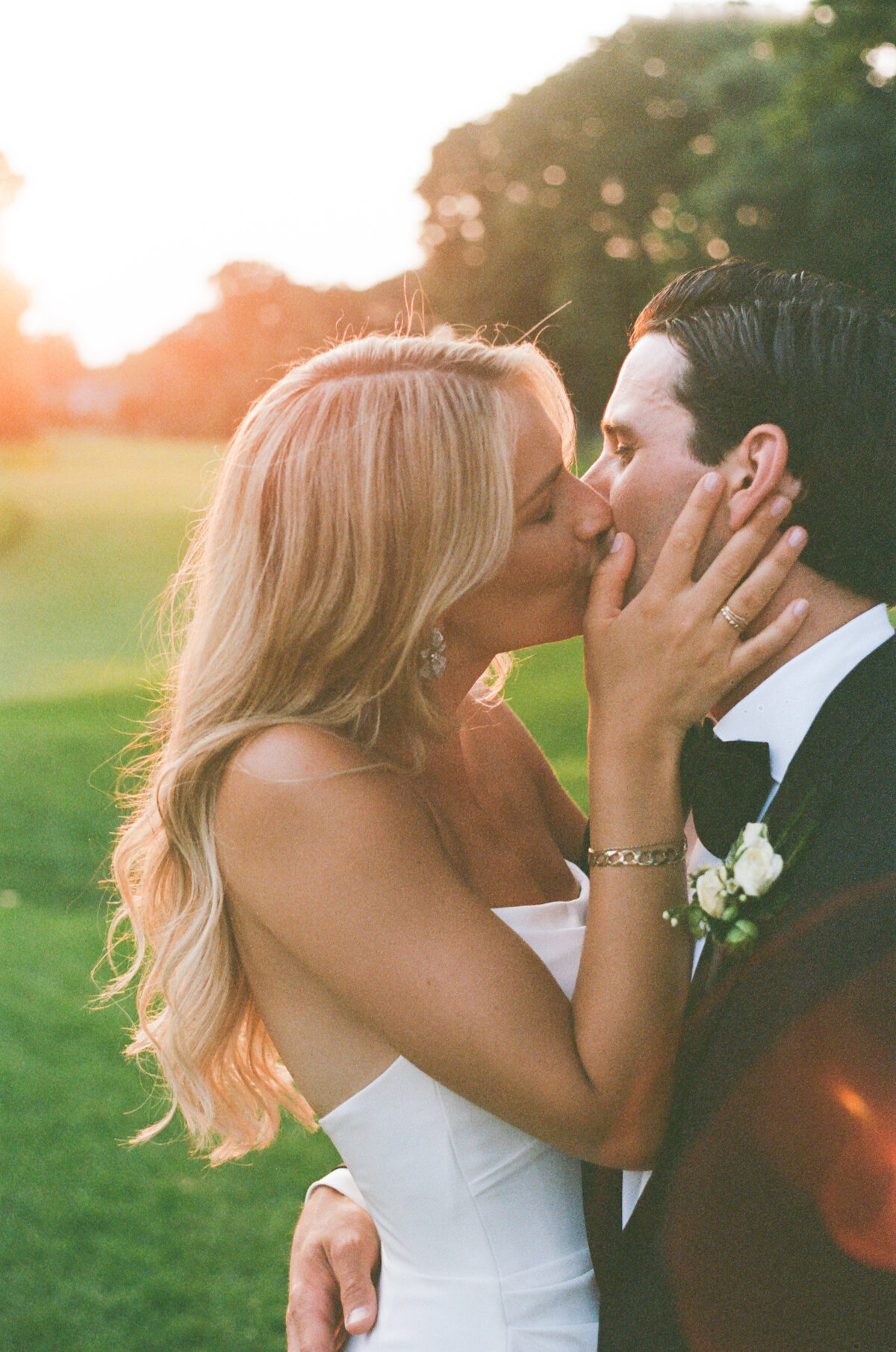 Blonde bride kissing a groom in a tuxedo at sunset on film