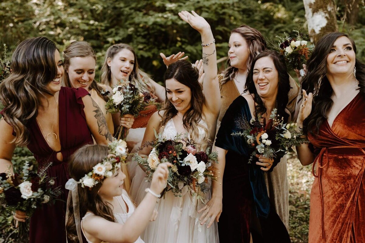 A bride and her bridesmaids all hold their bouquets and celebrate.