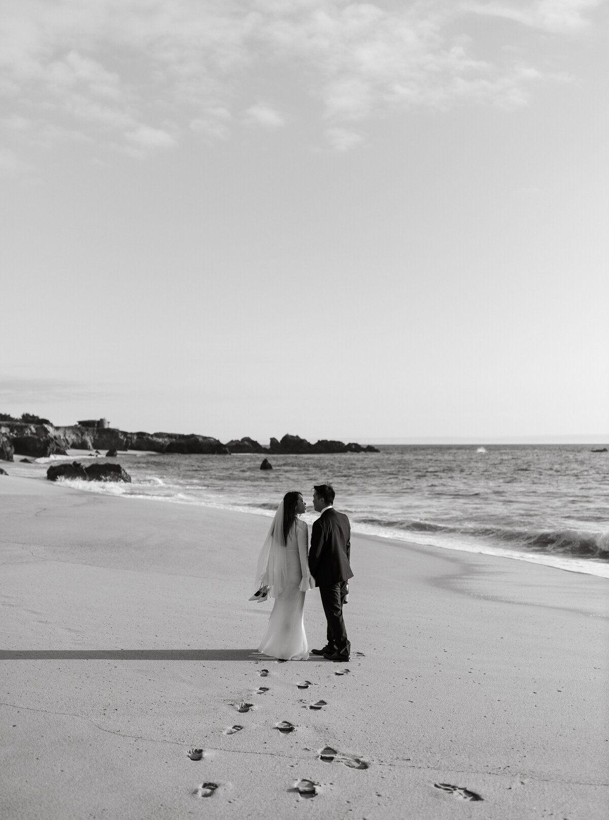 Wedding Photographer & Videographer, black and white image of bride and groom walking in the sand