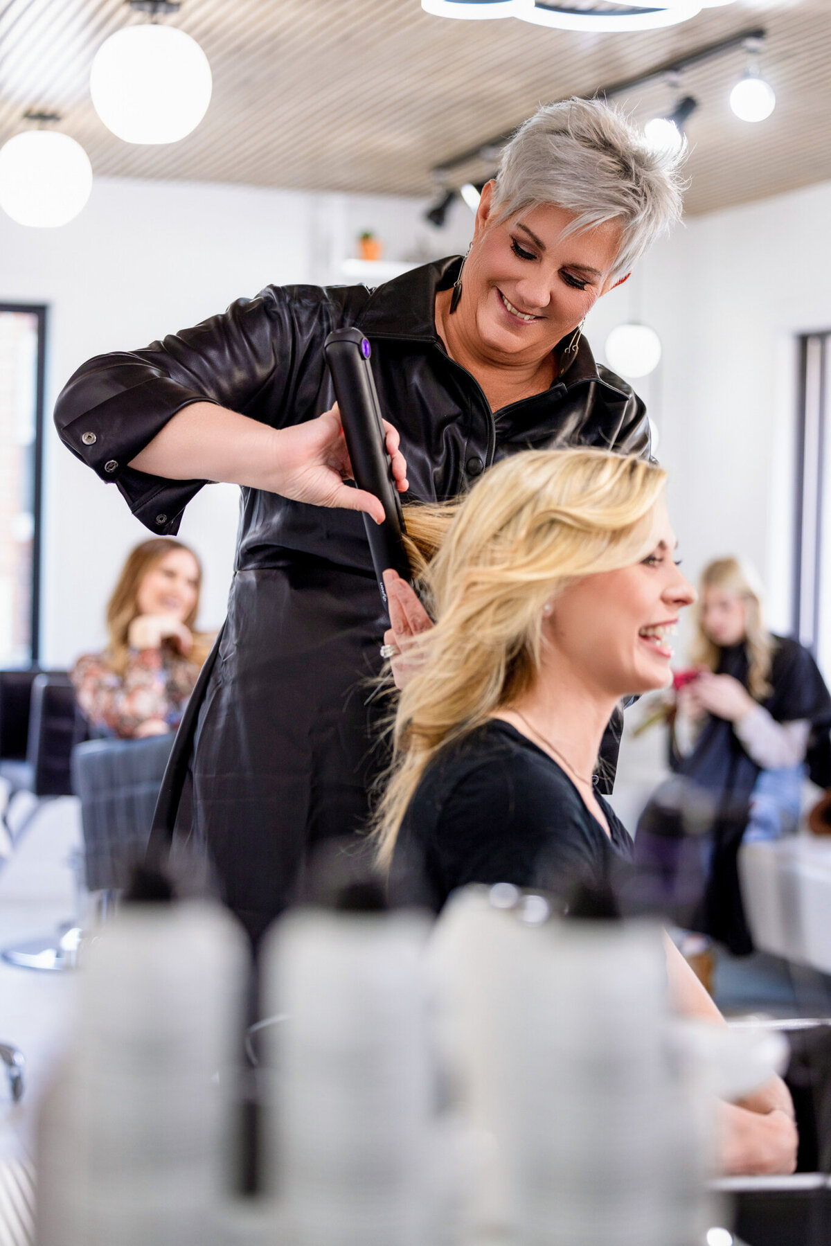 A stylist’s hands skillfully wrap hair around a curling iron, emphasizing technique and expertise. A great branding image for salons that pride themselves on attention to detail and high-quality styling.