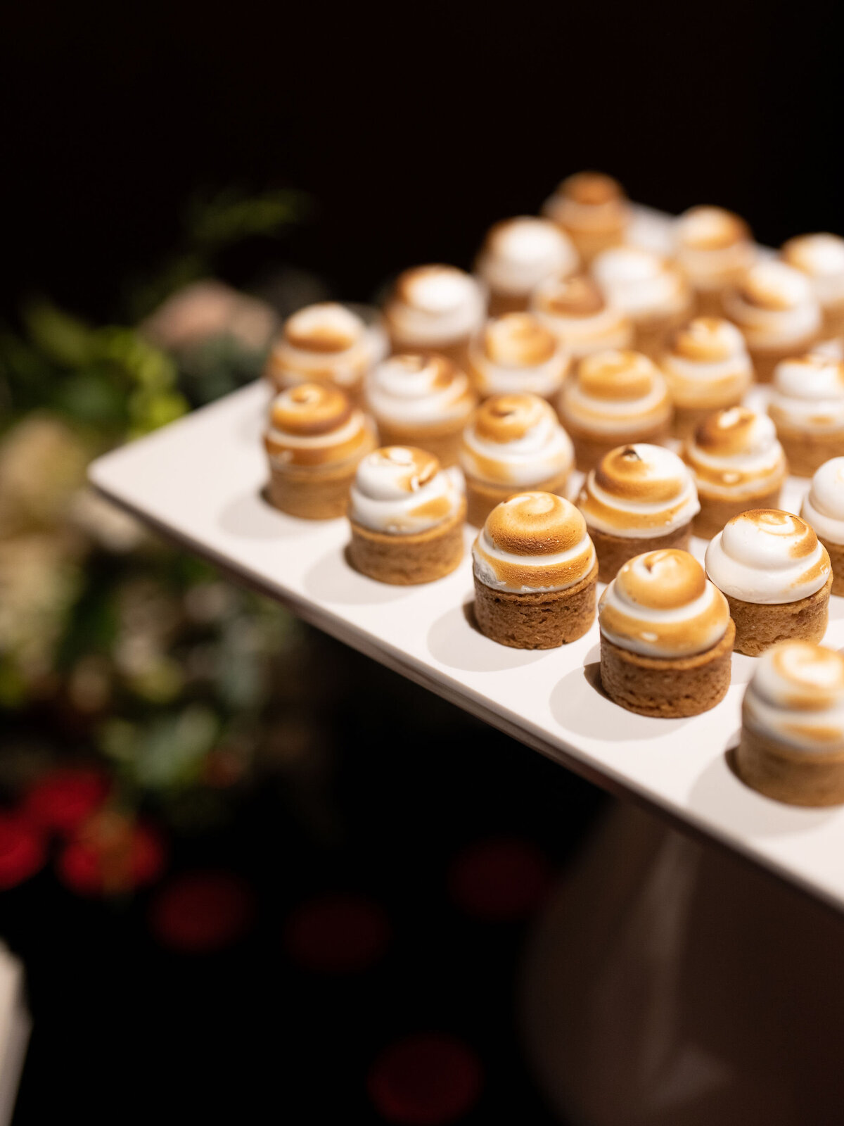 A close-up of a tray filled with beautifully arranged mini lemon meringue tarts, elegantly displayed at a wedding reception.