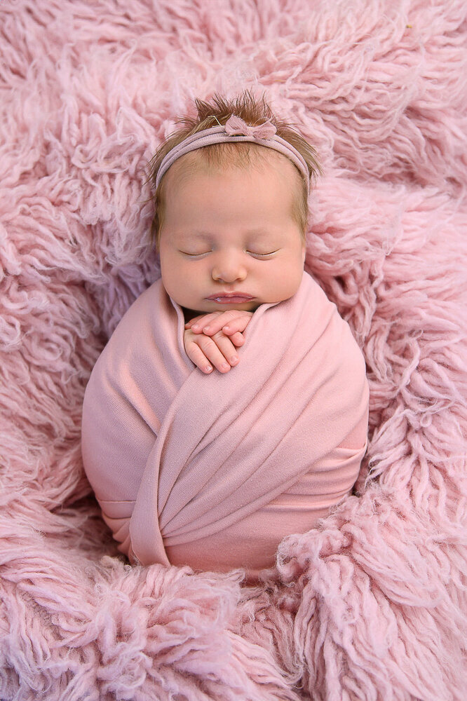 Baby girl wrapped in pink on a pink rug for her newborn photography session in Hamilton, Ontario.