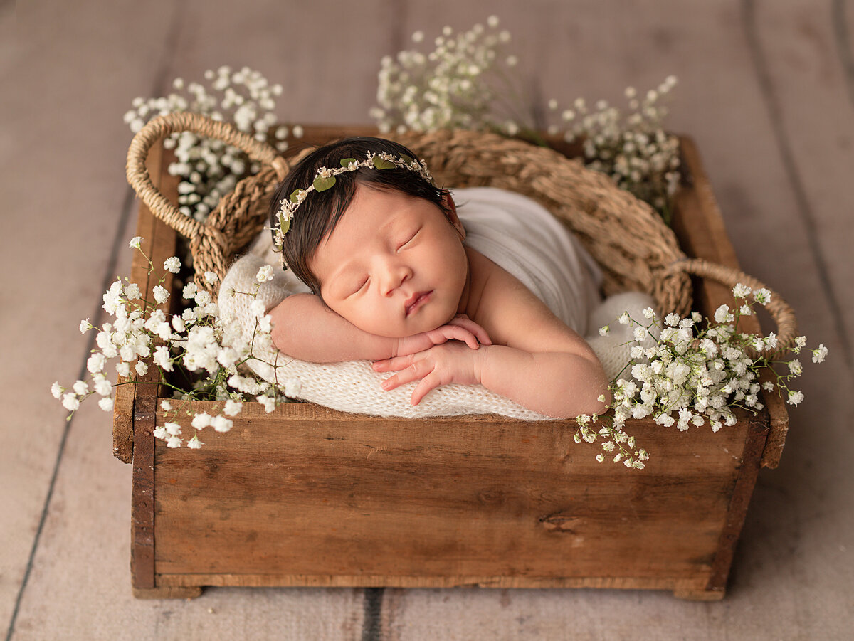 baby in wooden box with flowers around her