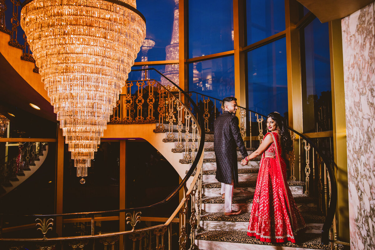indian christian bride and groom stand on the steps at leonards palazzo at night near the chandelier during the evening wedding reception