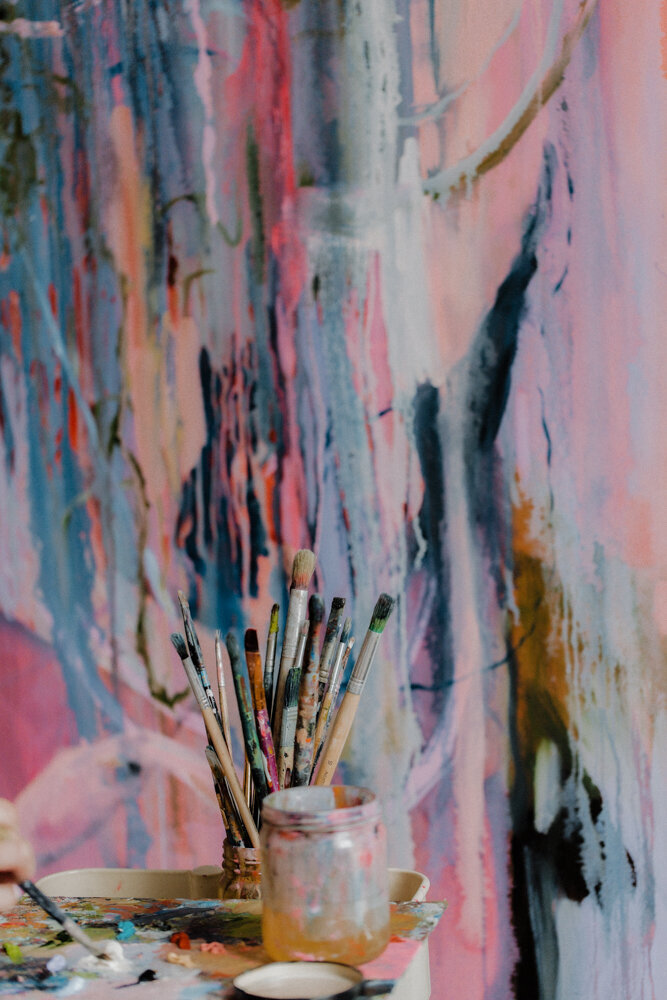 paint brushes in front of a painted canvas
