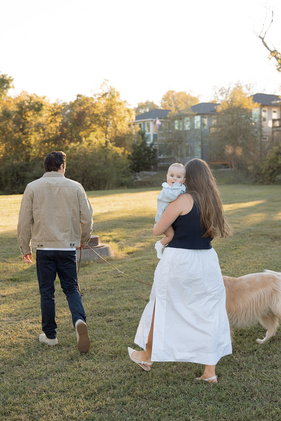 Infant looks over her mothers shoulder while family walks dog. 
