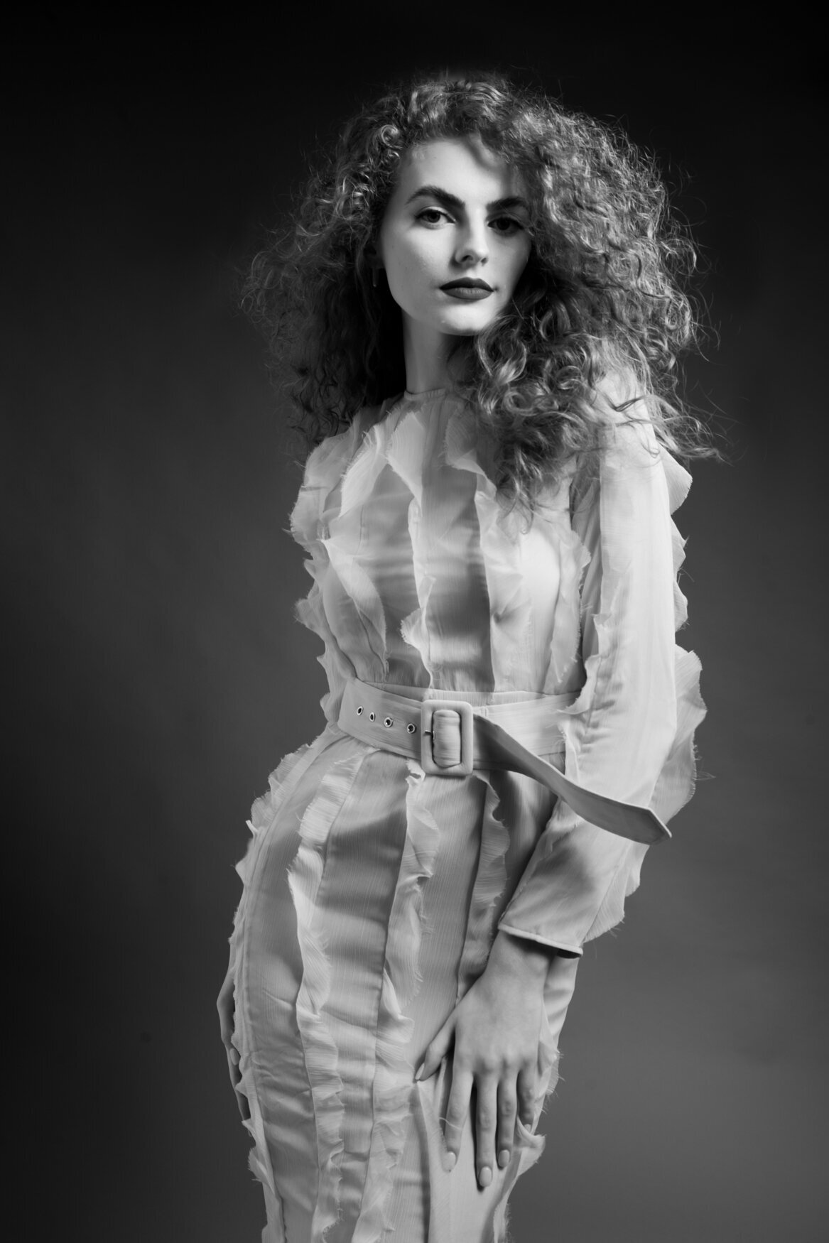 A woman standing confidently in front of the camera with a hand on her leg and her shoulder a little raised