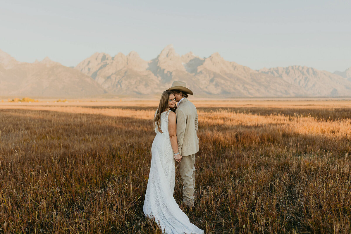 A couple doing bridal photos in a field in front of the Tetons in Grand Teton National Park