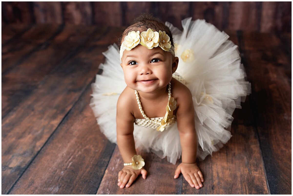 Beautiful little six month old girl crawling on the floor and looking up smiling.