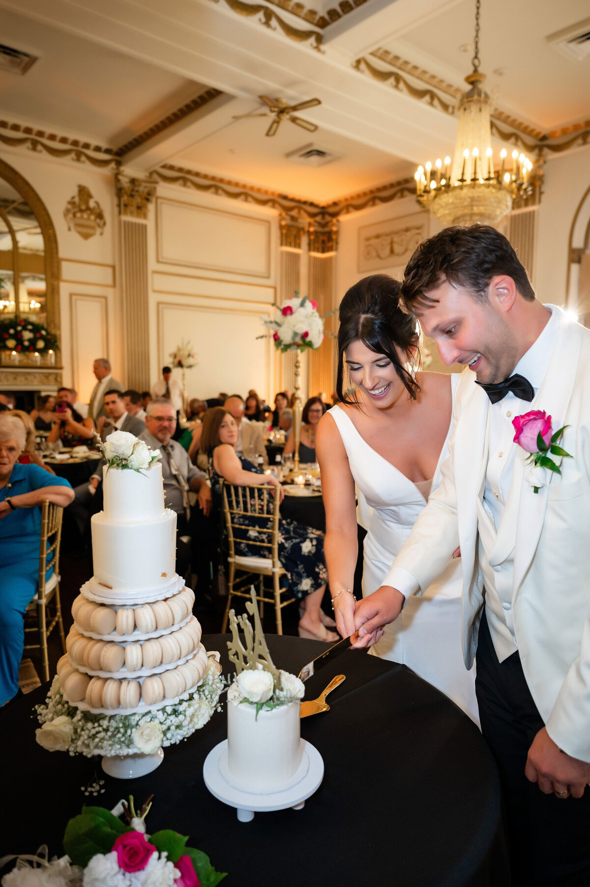 married couple cutting their wedding cake inside grand ballroom at george washington hotel both wearing white and smiling