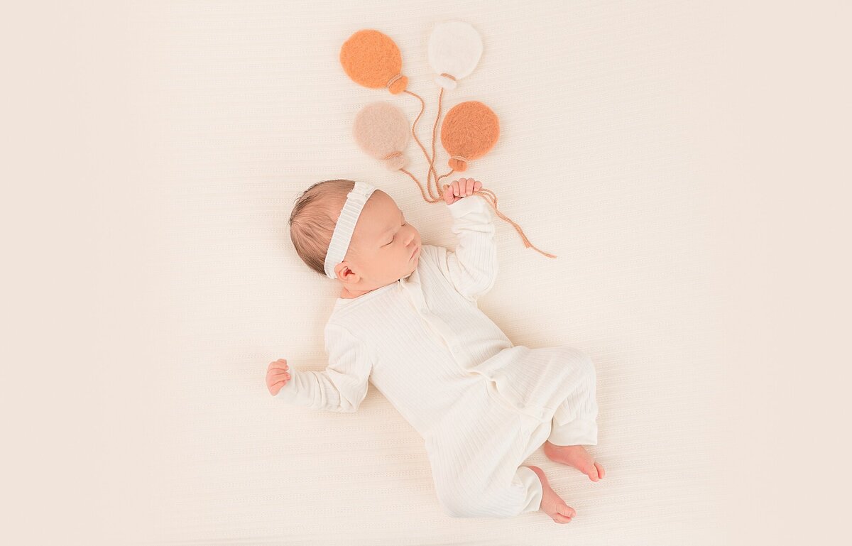 newborn baby holding balloons
