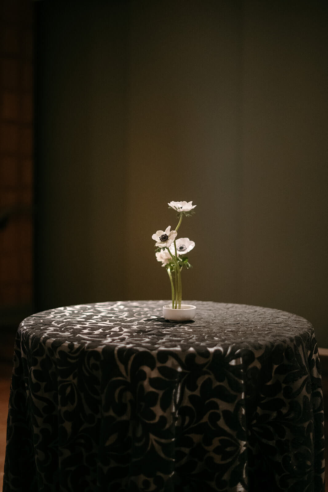 Cocktail table draped in a black textured linen showcasing a single vase of seasonal flowers at the St. Regis Aspen wedding cocktail hour.