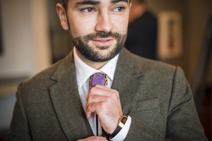 A groom glances off camera as he adjusts his tie on his wedding day.