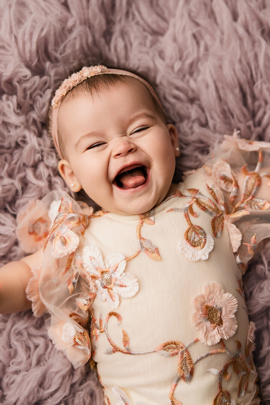 Cute Fort Collins six month old laughing while she's laying on a purple rug in a pretty outfit for photos