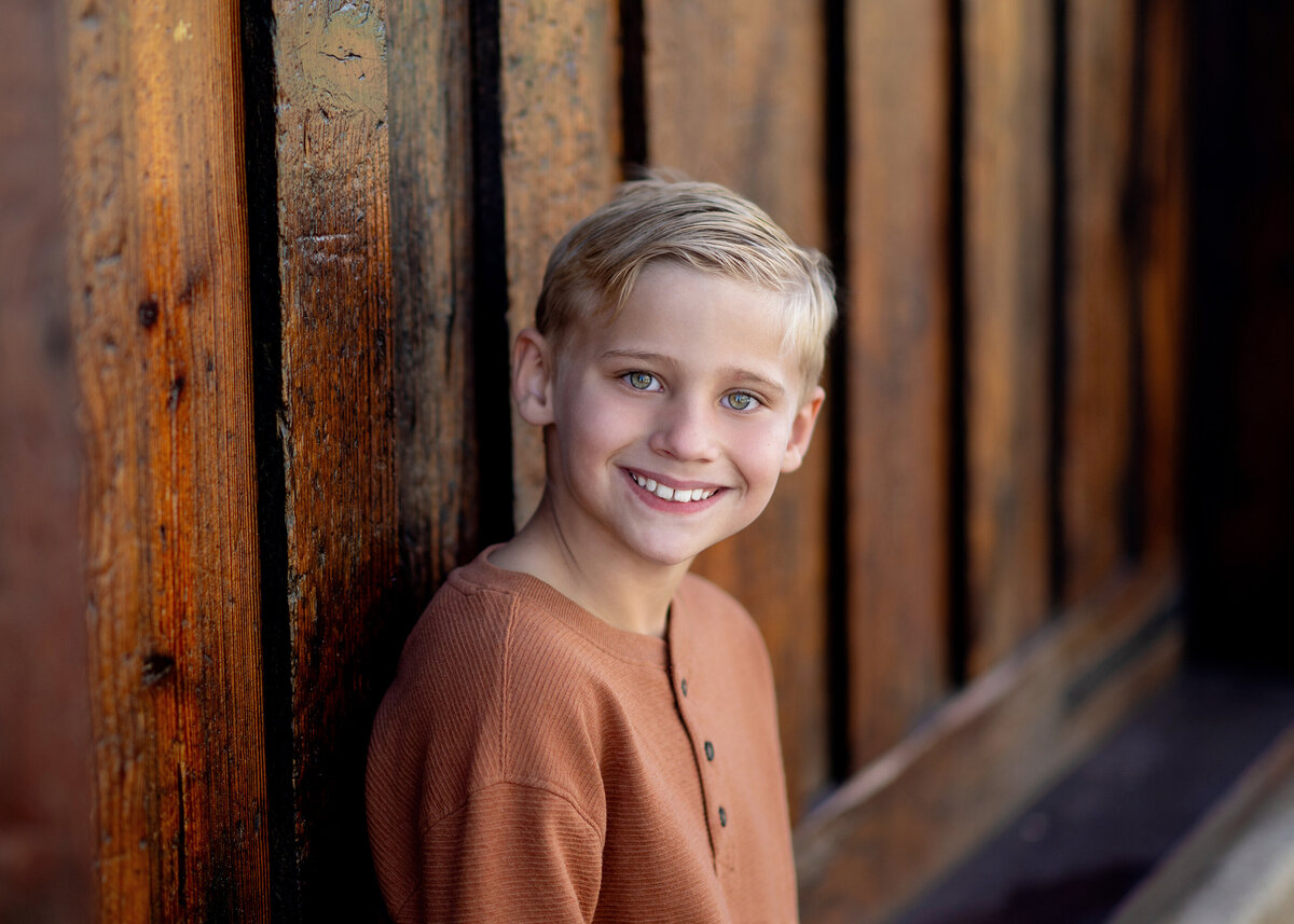 A child stands alone against a weathered wooden wall, their smile contagious
