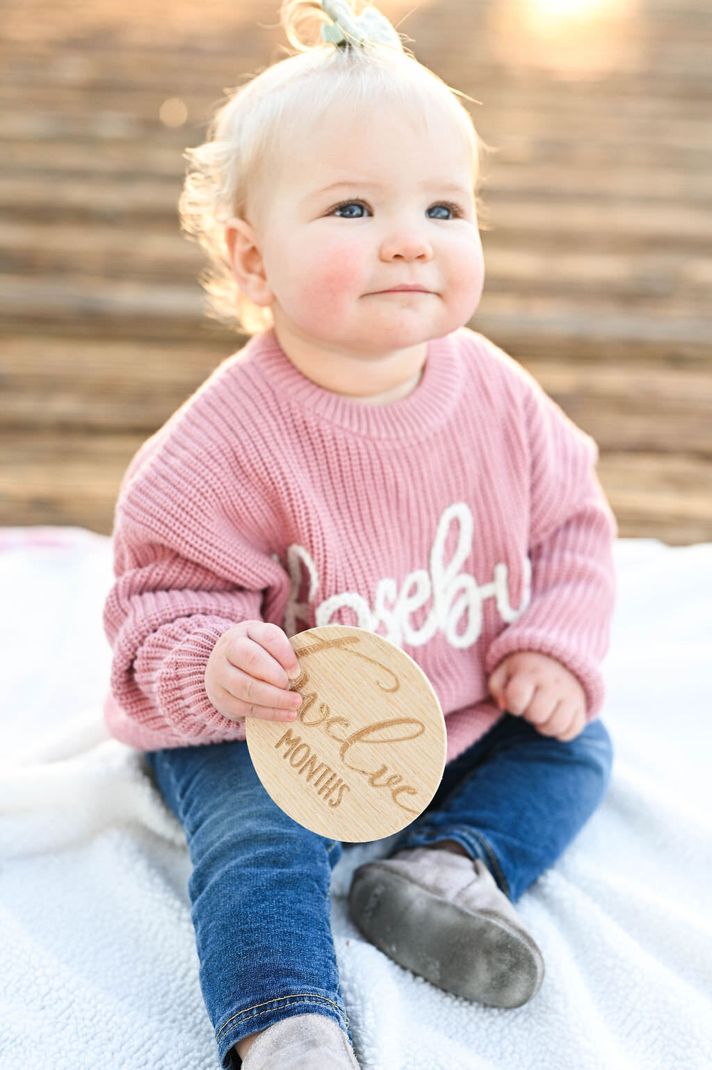 A baby holding a wooden circle that says "twelve months"