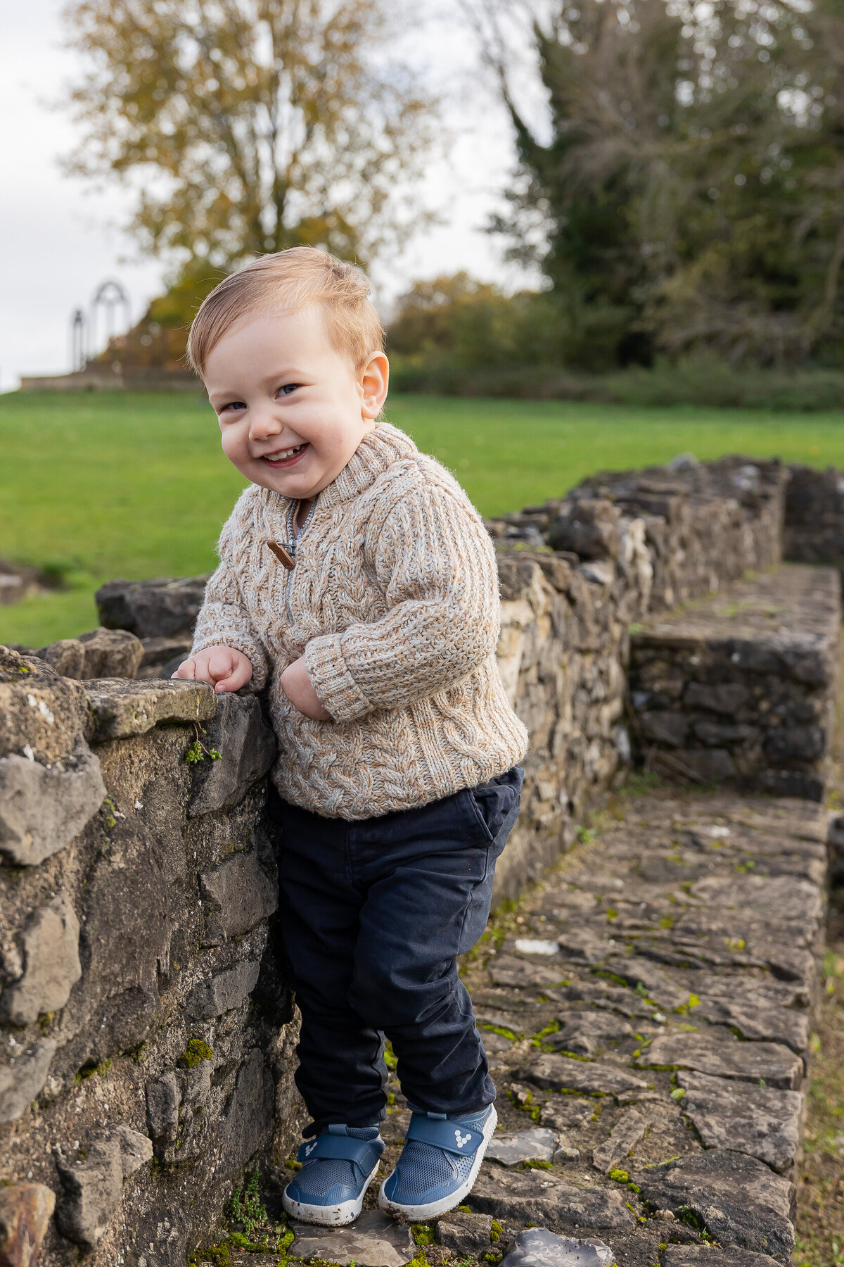 A baby boy is leaning against a stone wall during a photography session.