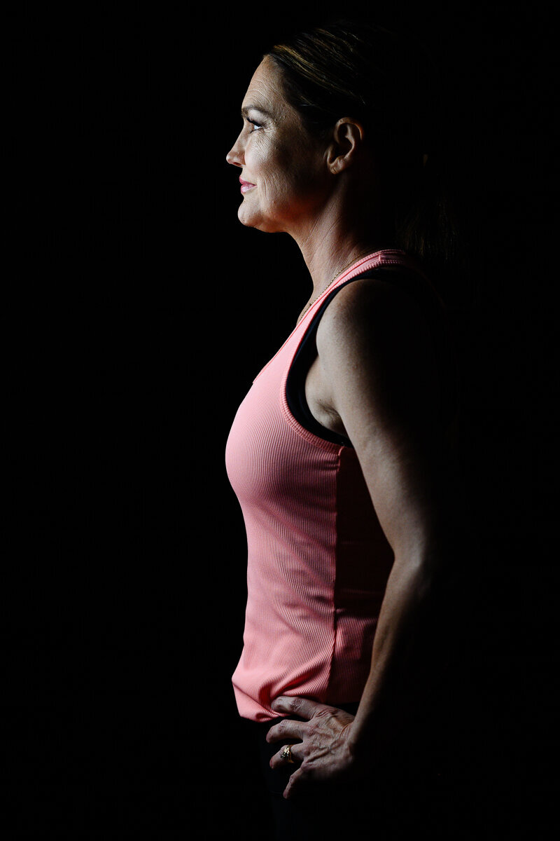 Branding photography for a woman standing with a black background and her side view illuminated by light during her fitness branding photo shoot with a Denver brand photographer.