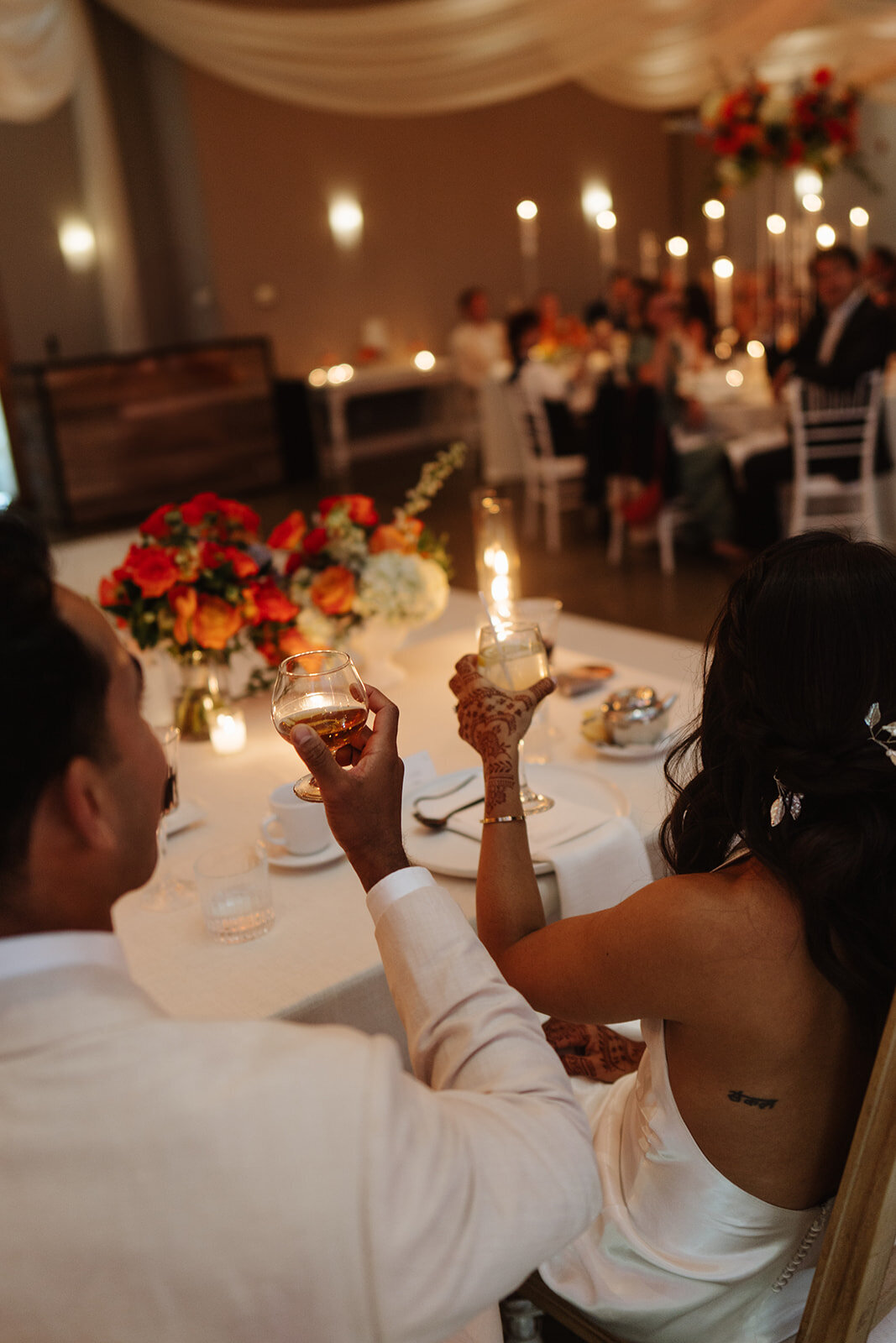 Bride and groom at a candlelit reception table — intimate wedding dinner surrounded by warmth and laughter.