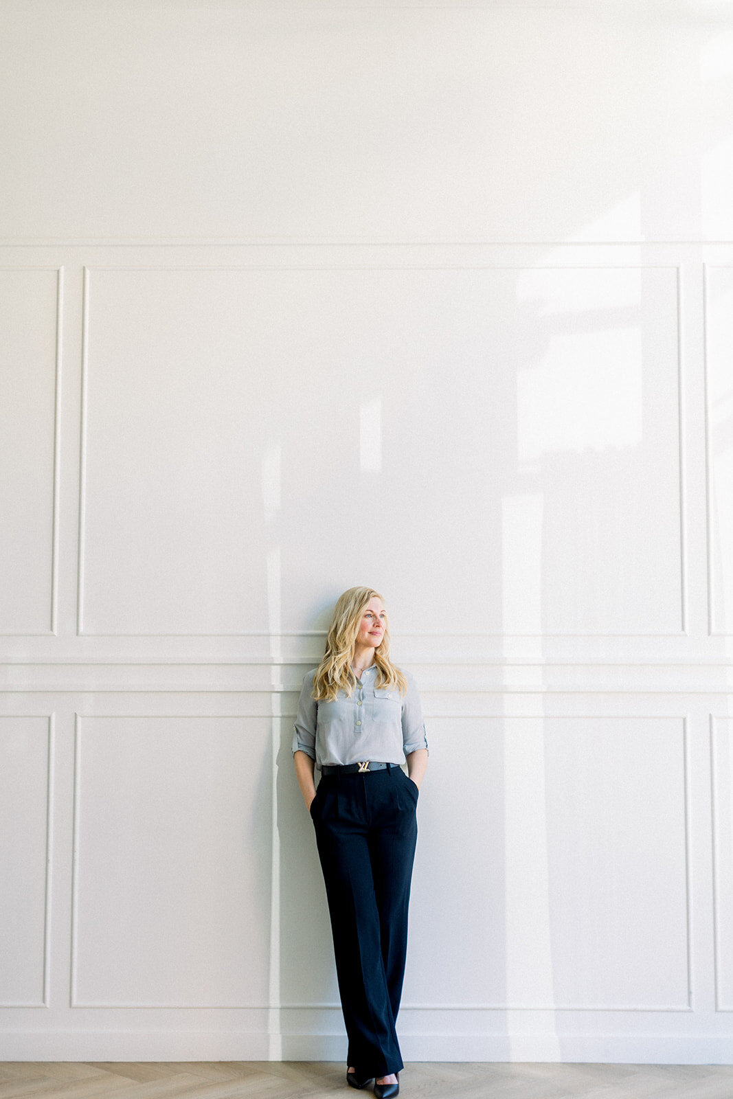 Brand photo of a blonde Calgary business woman leaning casually against a white wall