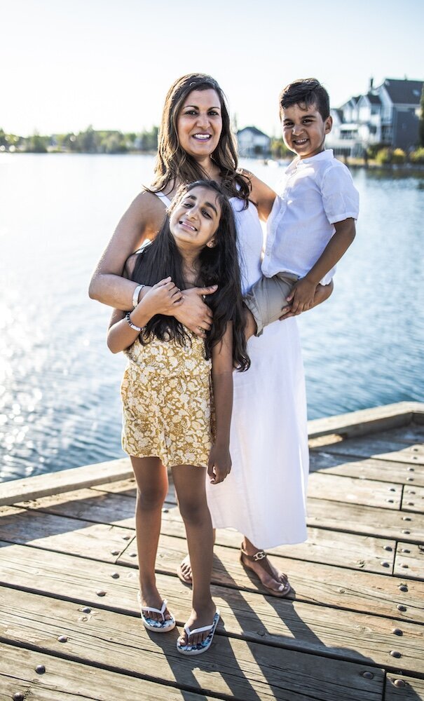 A mom in a white dress is holding her son on her hip and hugging her daughter with her other hand