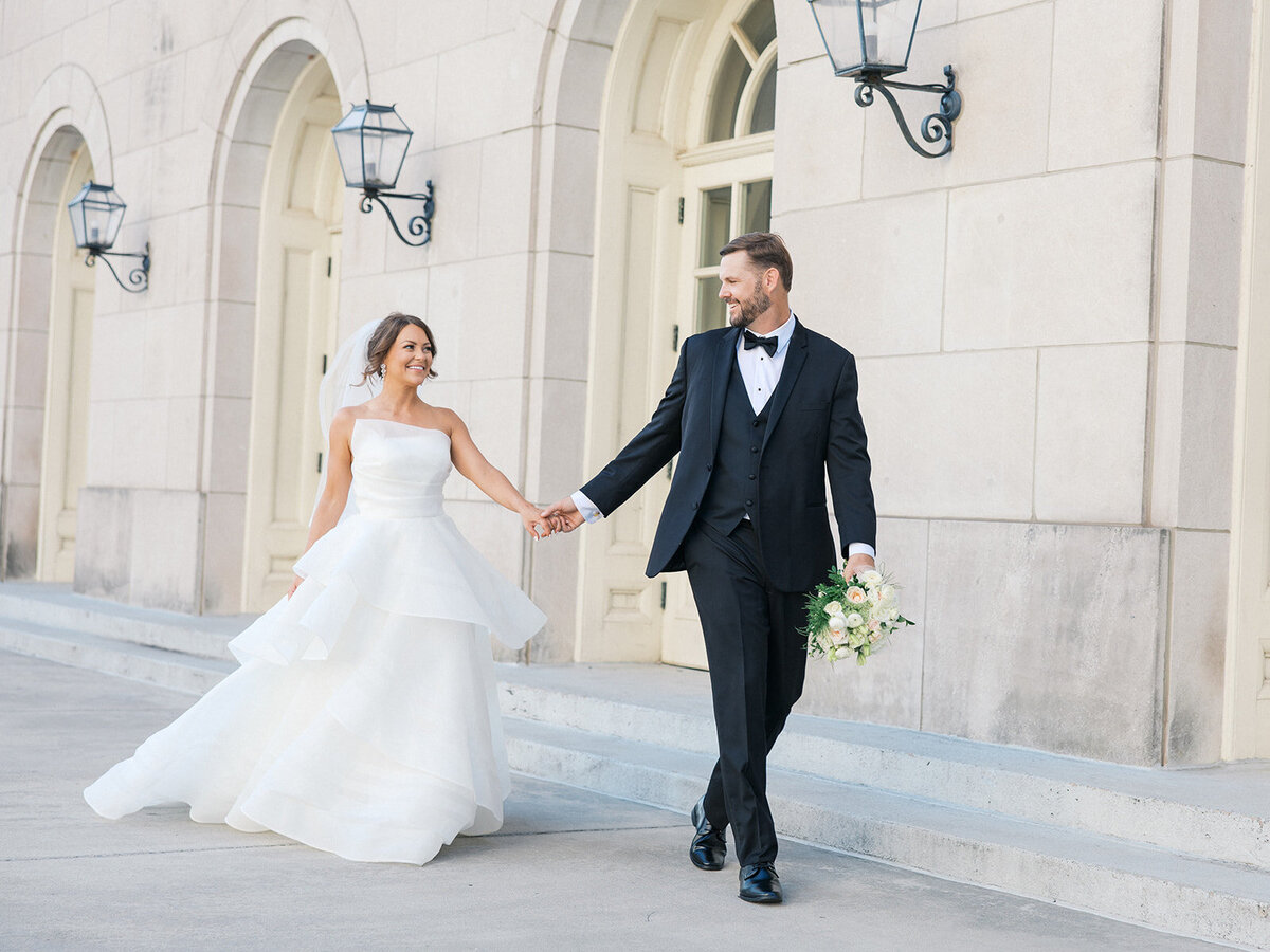 Bride follows groom in black tux walking in front of European style wedding venue in Georgia