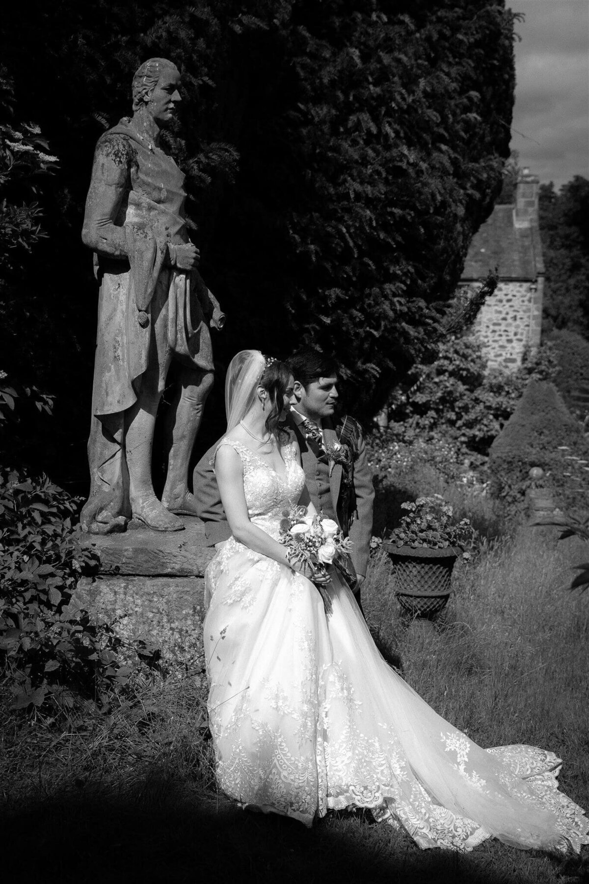 Bride and groom sit in front of a statue at a Scottish castle.