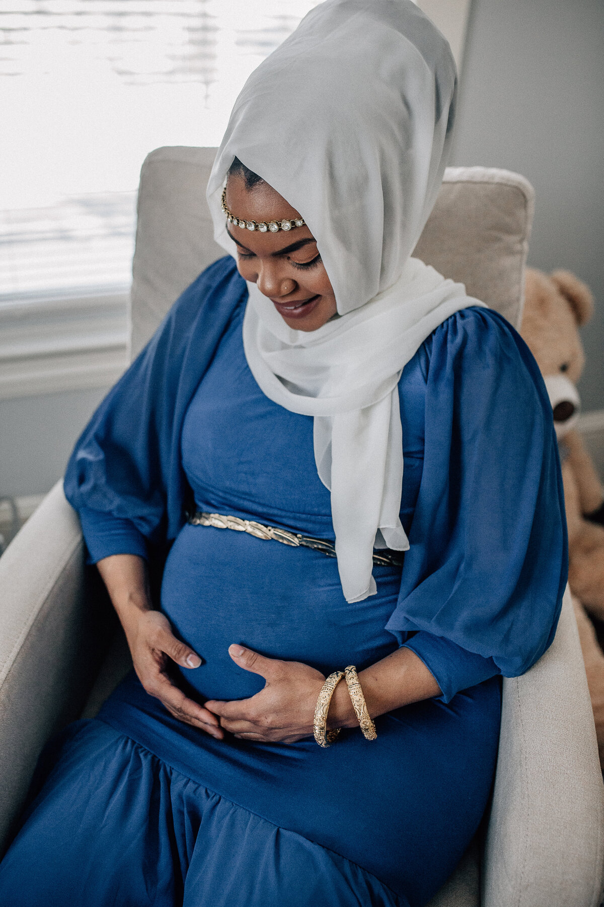 Pregnancy photoshoot with soon to be mom sitting in chair, holding her belly.