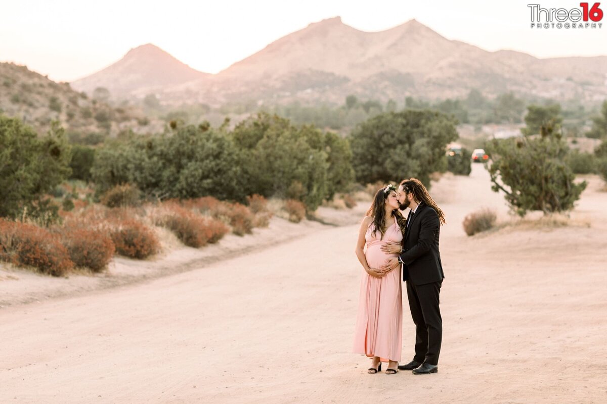 Parents to be share a kiss in the dessert at Vasquez Rocks