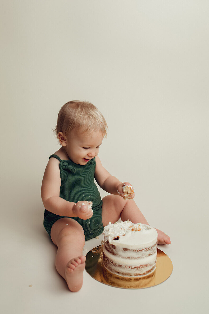 a one year old boy with fist fulls of vanilla cake during a cake smash session at lulu belle photography in rochester ny