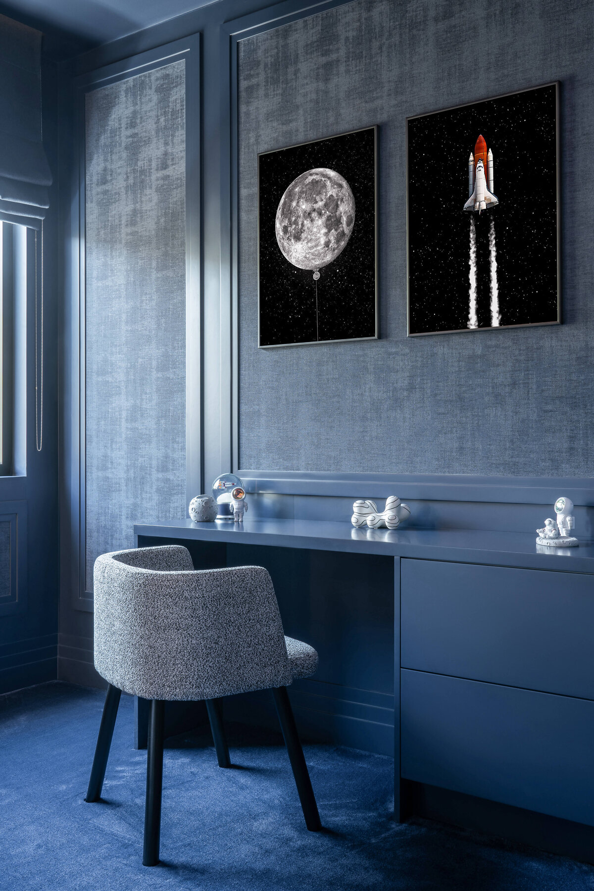 A blue built-in desk in a boy's bedroom. Above the desk are photos of the moon and a rocketship.