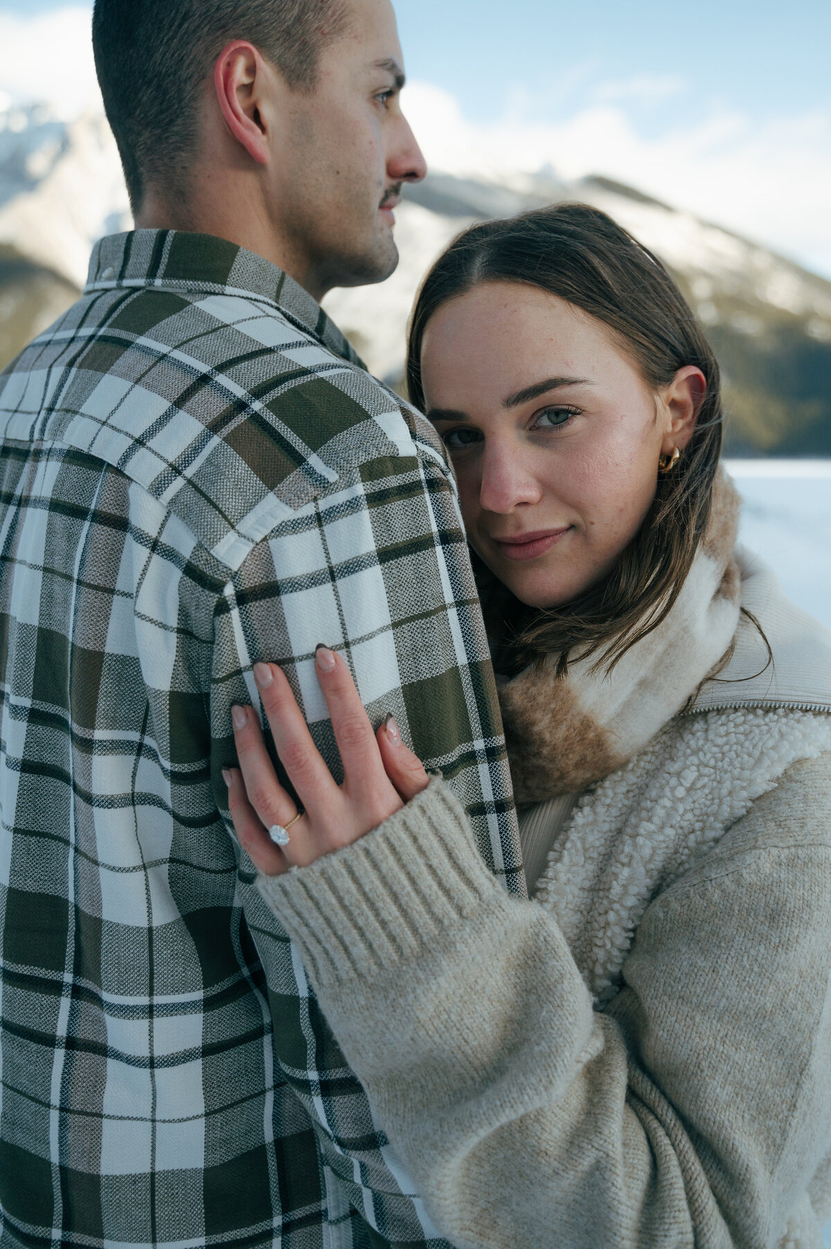 Woman smiles while hugging her fiance, showing off her engagement ring during a mountain engagement session in Banff.