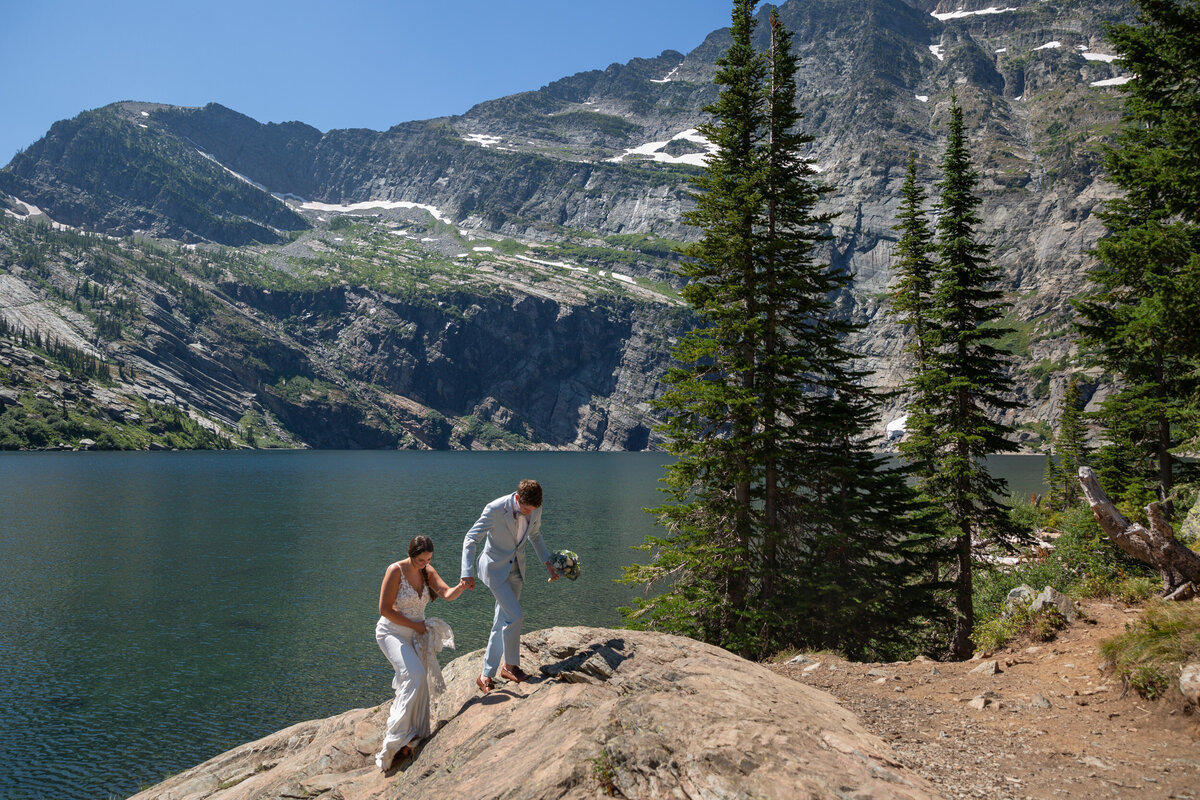A bride and groom walk up a rocky hill next to a lake on their Montana elopement day.