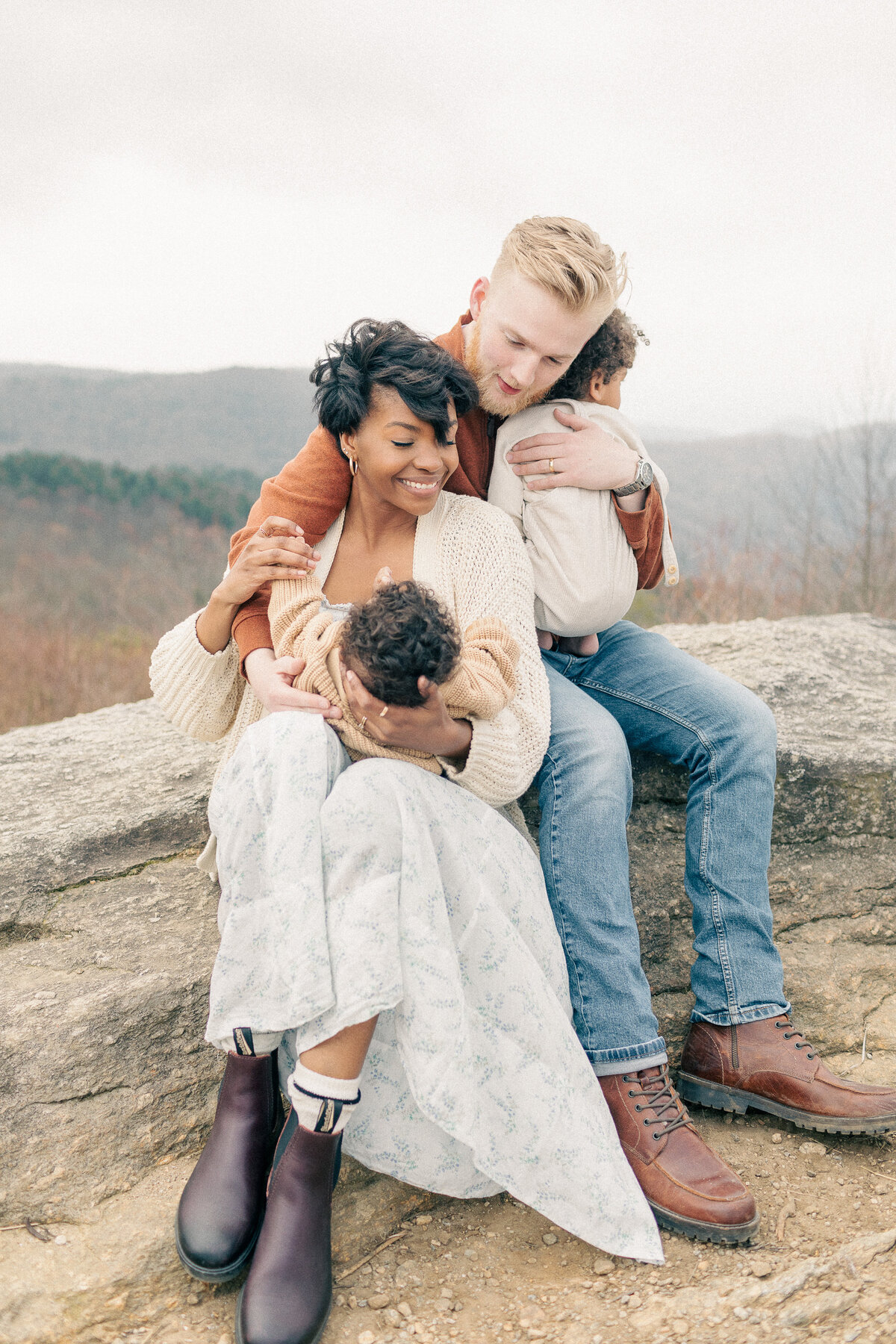 Parents sit with their two babies nestled in their arms during an outdoor newborn session at a Kansas City overlook.