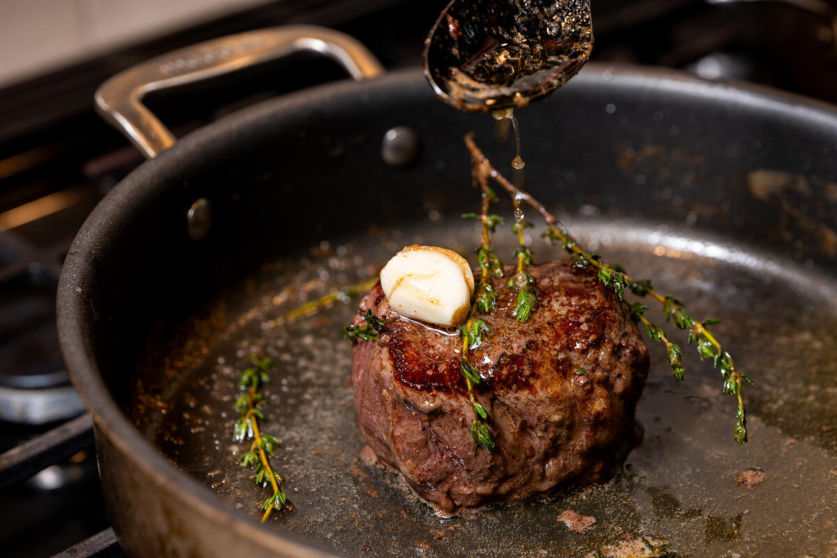 Butter being basted over a small steak in a pan 