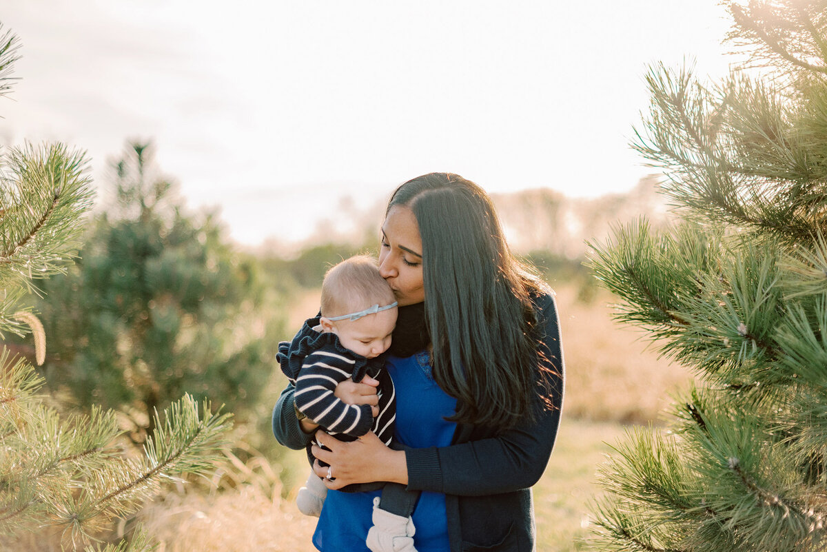 Mom kissing her baby daughter at a Christmas tree farm