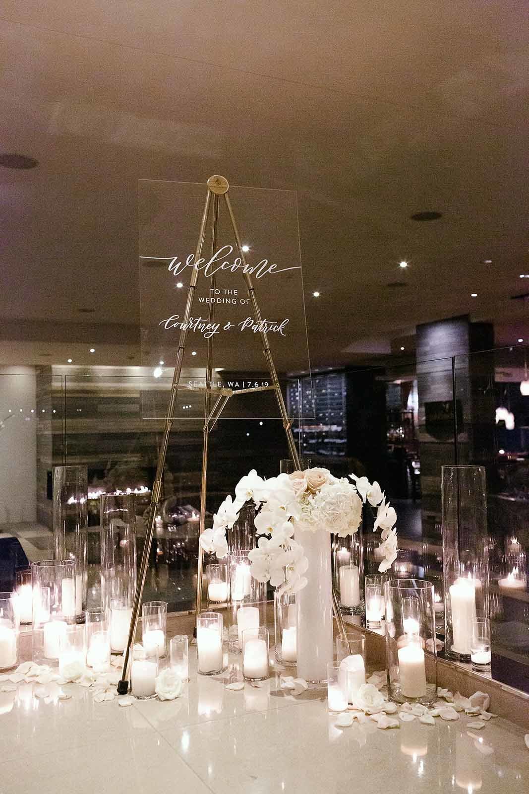 elegant welcome sign in clear lucite on gold stand, with orchid arrangements and candles at base