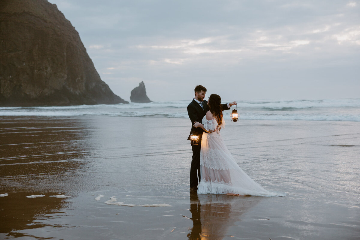 Newlyweds embrace on a beach while holding lanterns at sunset for Portland Wedding Photographers