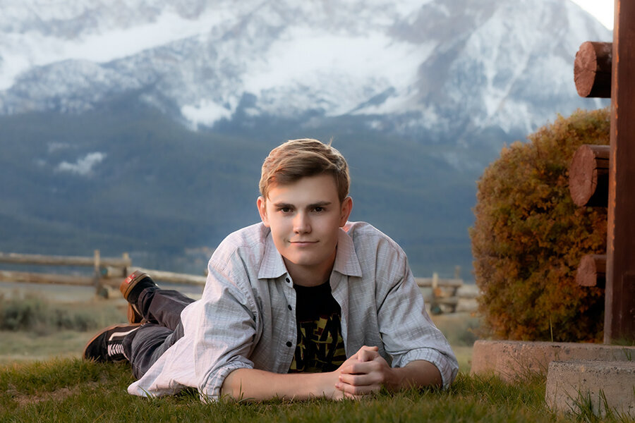 High school senior laying on ground propped up by elbows with snow capped mountains in background.