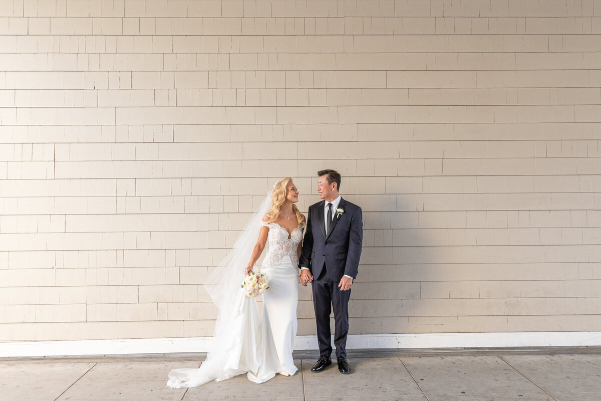 A bride and groom holding hands and smiling at each other