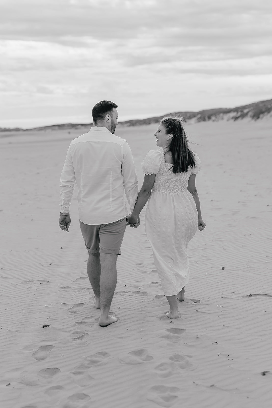 Couple walk away slowly holding hands on the beach at Camber Sands