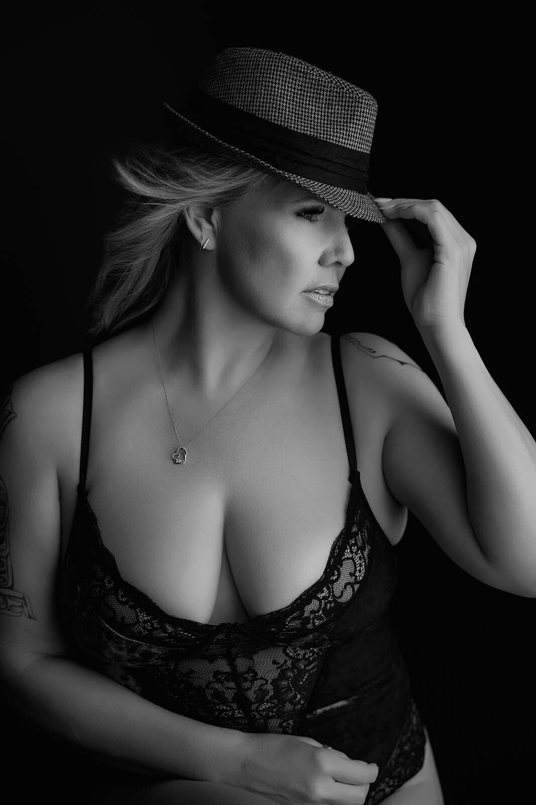 Looking down and holding her hat a Vancouver Boudoir Photographer poses a woman
