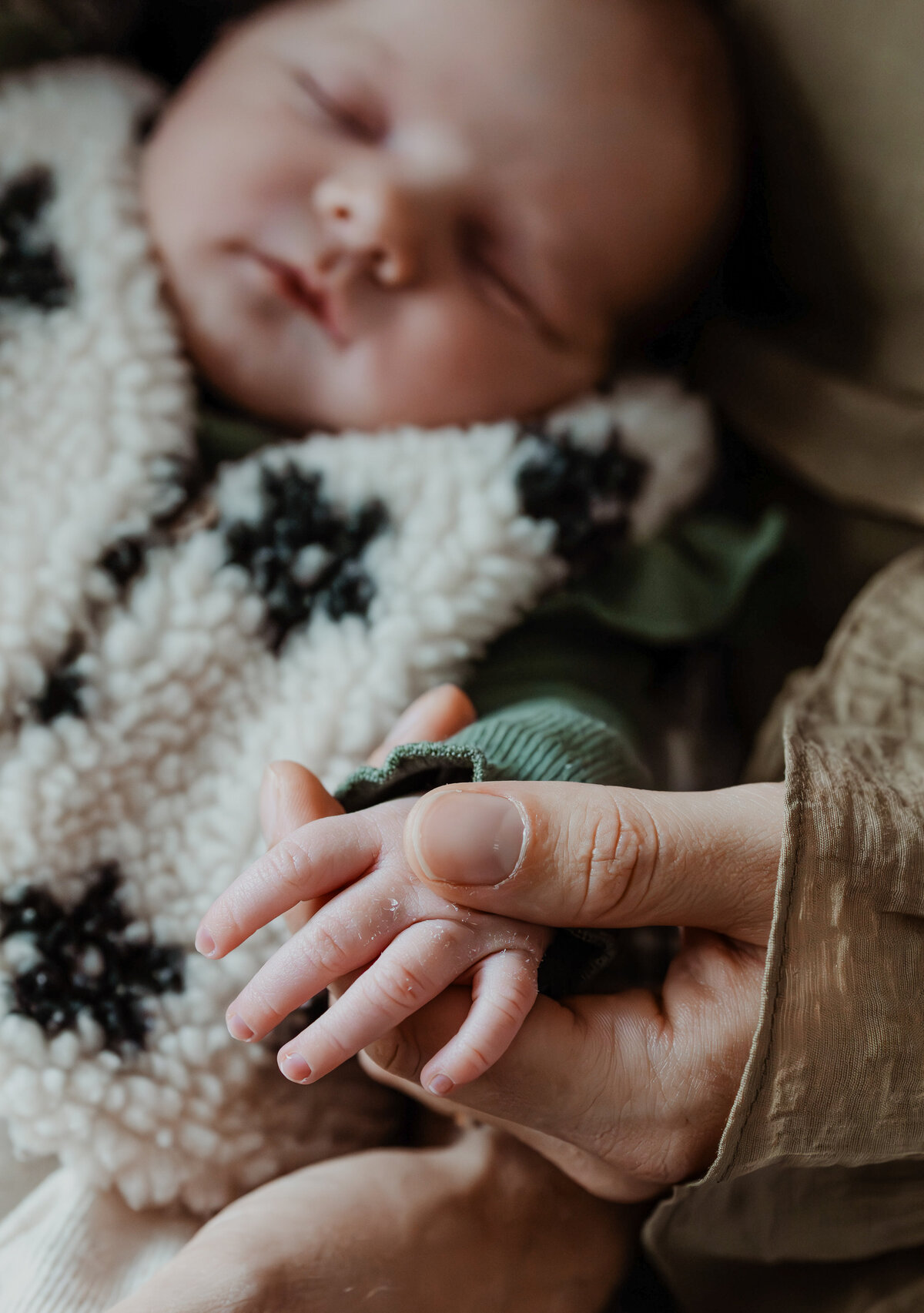 hand van mama die het handje van de baby vasthoudt met baby op de achtergrond
