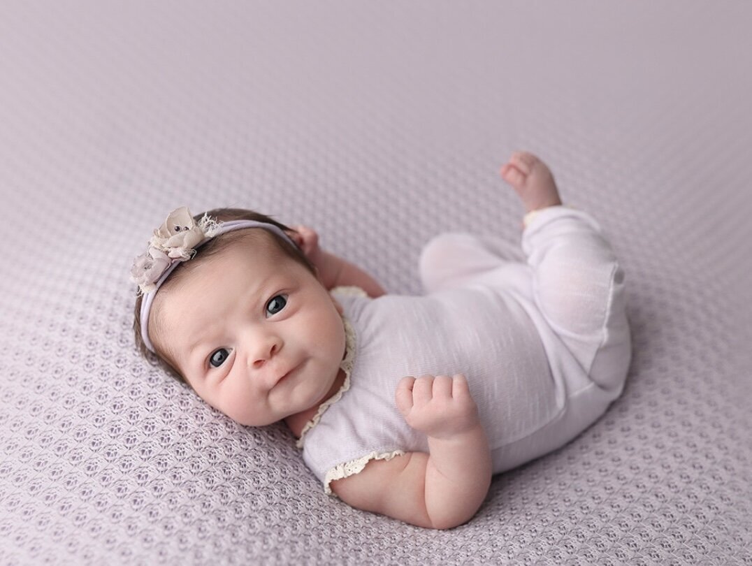 2 week baby girl all in purple and lying up awake on a purple bubble blanket.