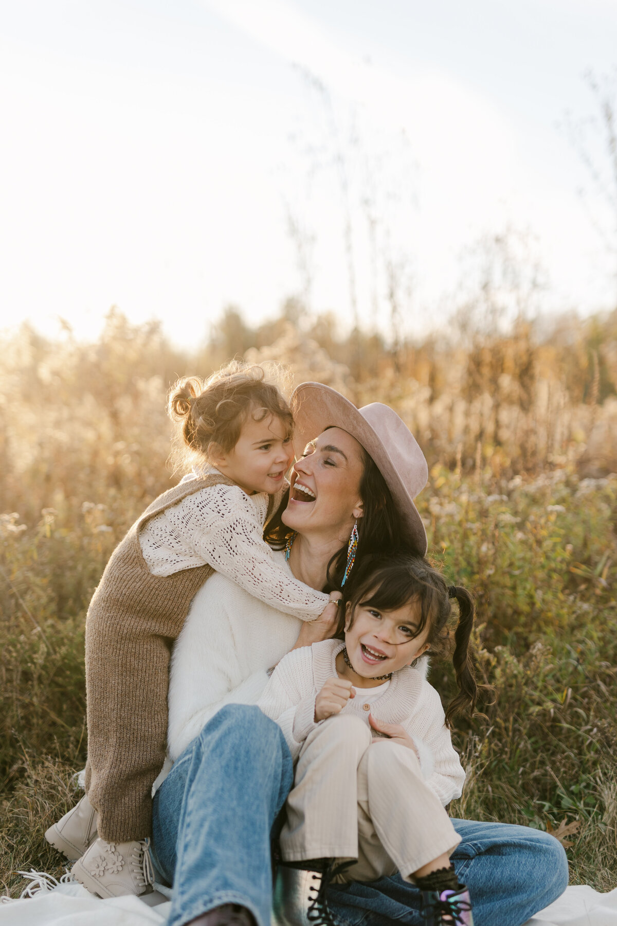 A mother is smiling at her younger daughter while her oldest is sitting on her lap at a Toronto family session