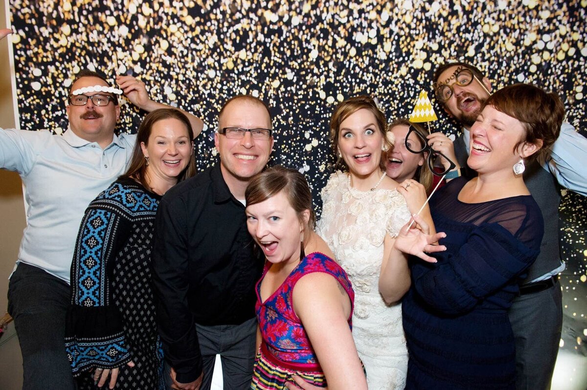 a group of wedding guests act silly in front of a glittery backdrop