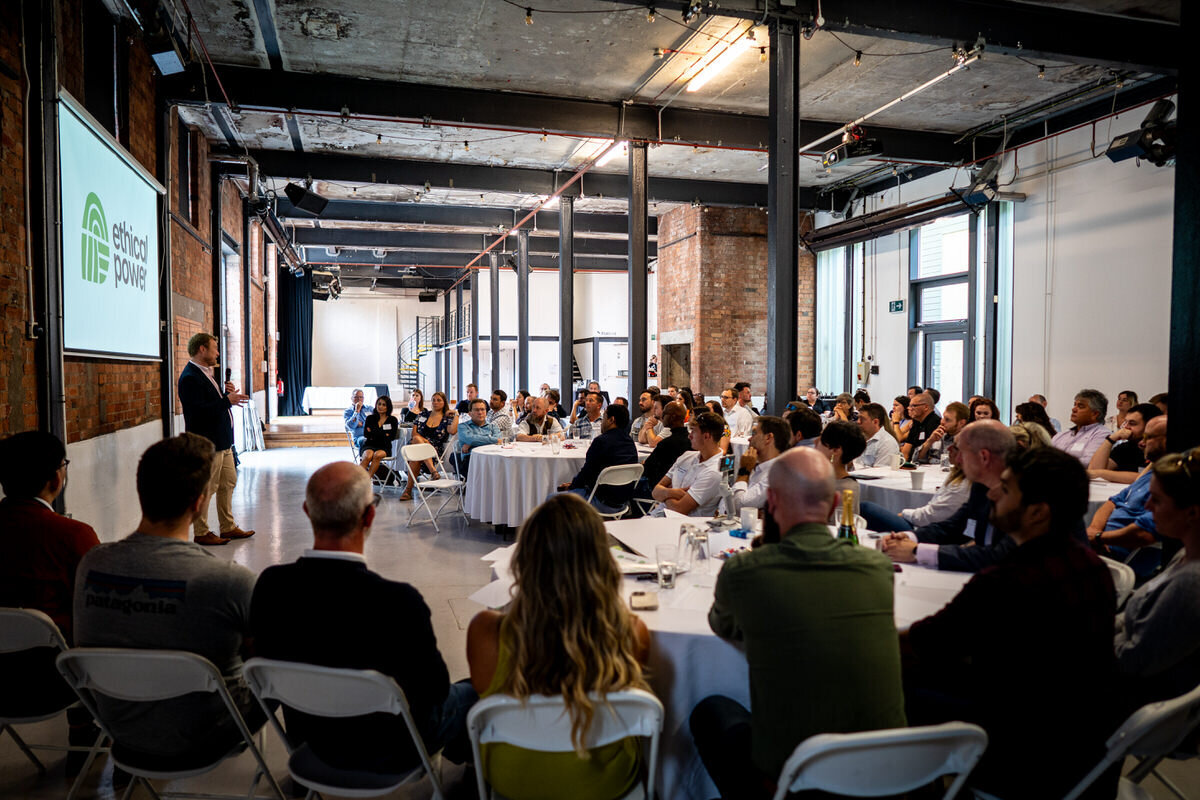 a tired dog looking directly at the camera under a bench whilst his owners muddy wellies are either side