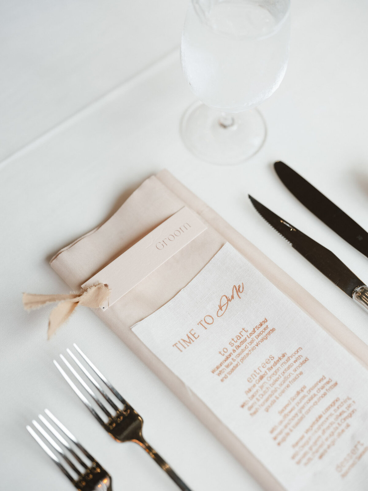 custom calligraphy wedding menu with flatware placed on a napkin on a wedding tablesetting representing full service design and calligraphy by Life in Letters.